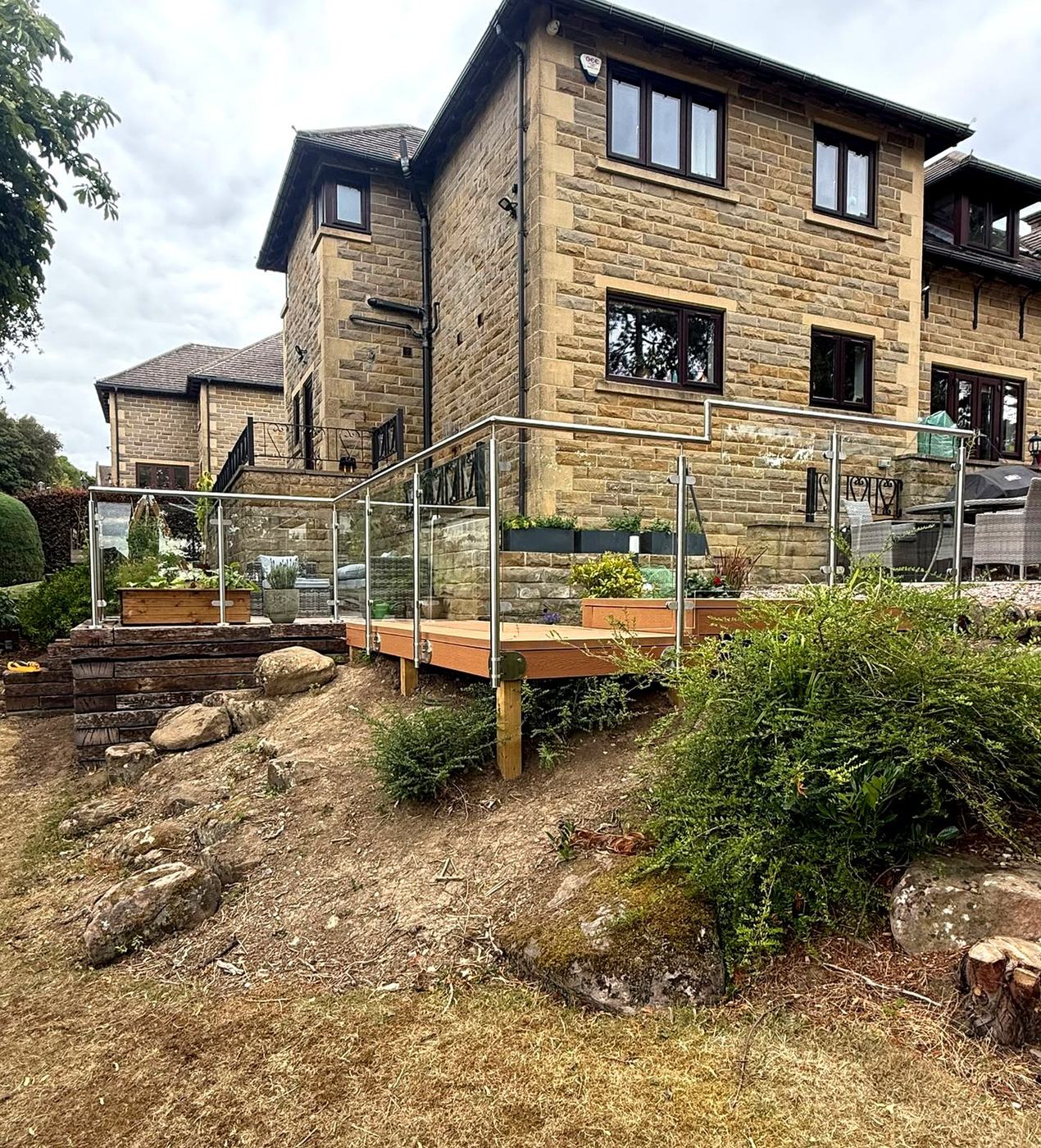 Stainless steel and glass balustrade running along a raised terrace at a stone house, Totley, Sheffield